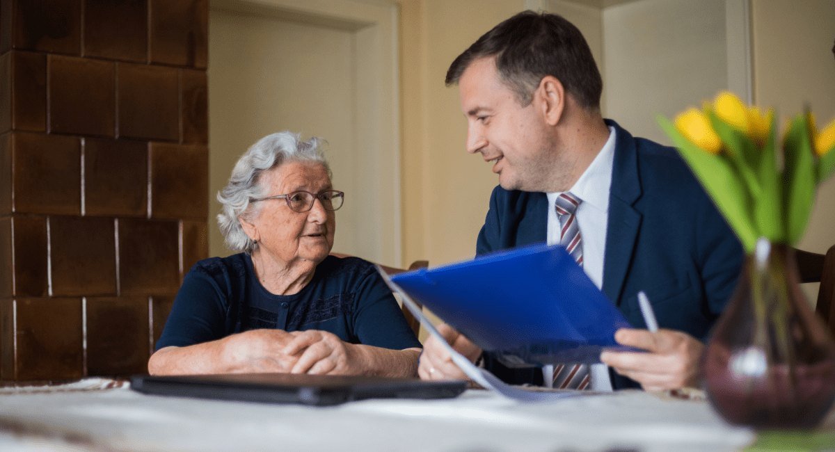 Senhora idosa conversando com um homem de terno que segura uma pasta azul