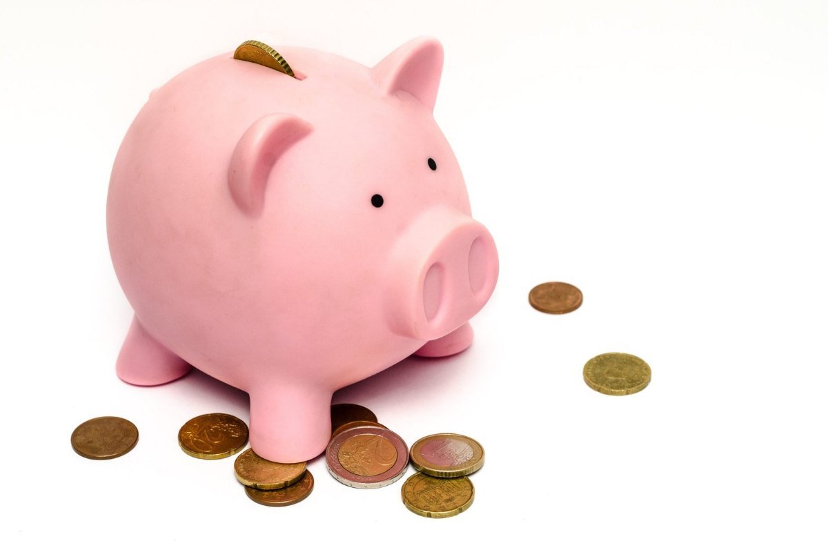 Cofrinho cor-de-rosa em forma de porco, com moedas em volta